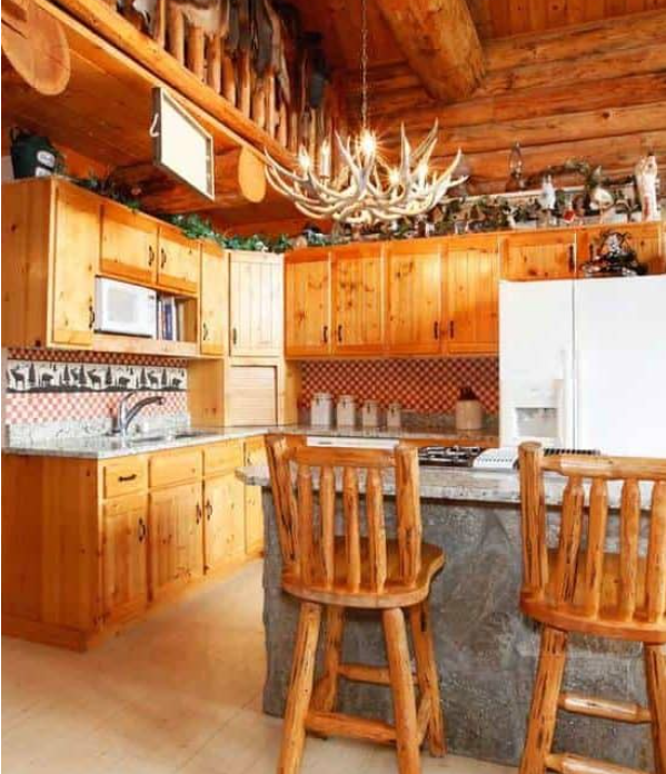 Bright kitchen room with rock counter cabinet, rustic counter stools, horn chandelier in a log cabin chalet